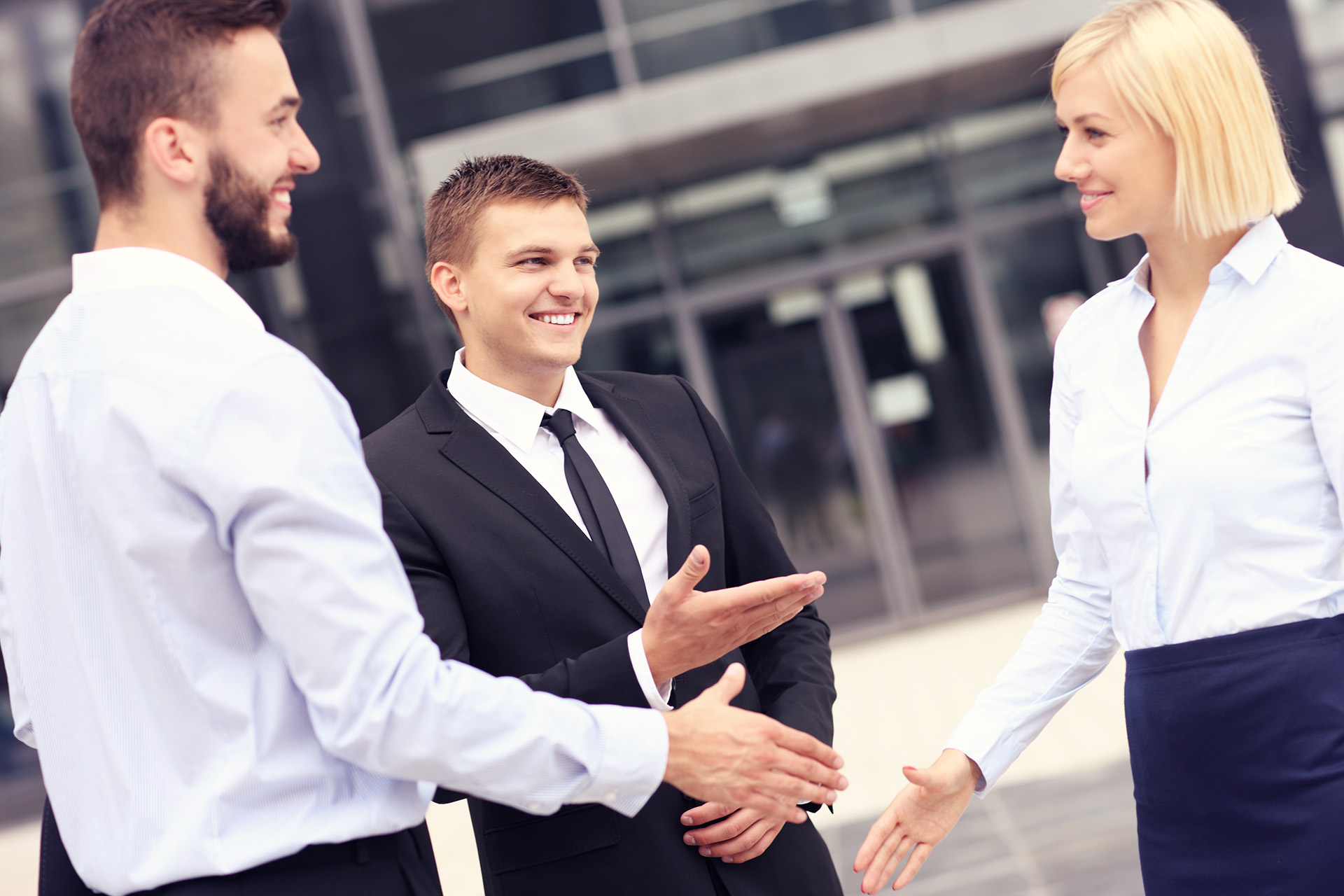 Zwei Männder und eine Frau im Business-Look reichen sich die Hände